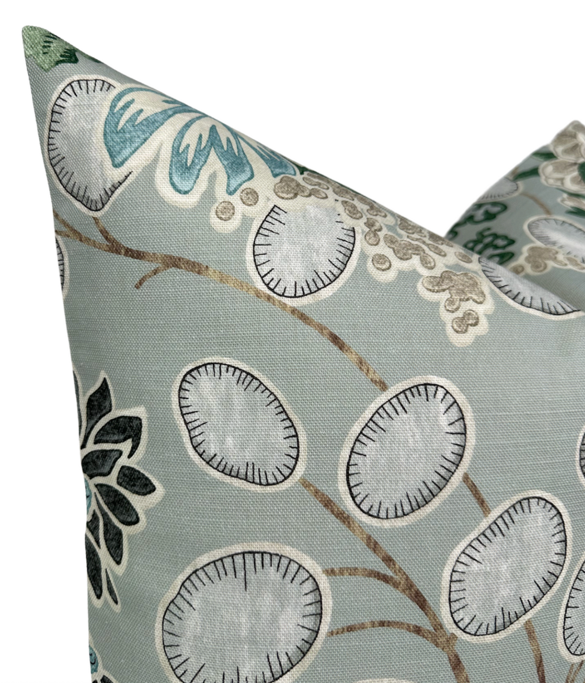 Close-up of a sage green pillow cover with embroidered floral and leaf patterns in shades of white, blue, black, and beige on a textured fabric.