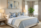 Bedroom with beige upholstered bed dressed in light blue and cream bedding, featuring three blue and beige floral pillows and light beige curtains framing two windows.