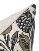 Corner of a beige fabric pillow cover featuring a pattern of black and gold pomegranate-inspired floral designs with detailed seeds and leaves.