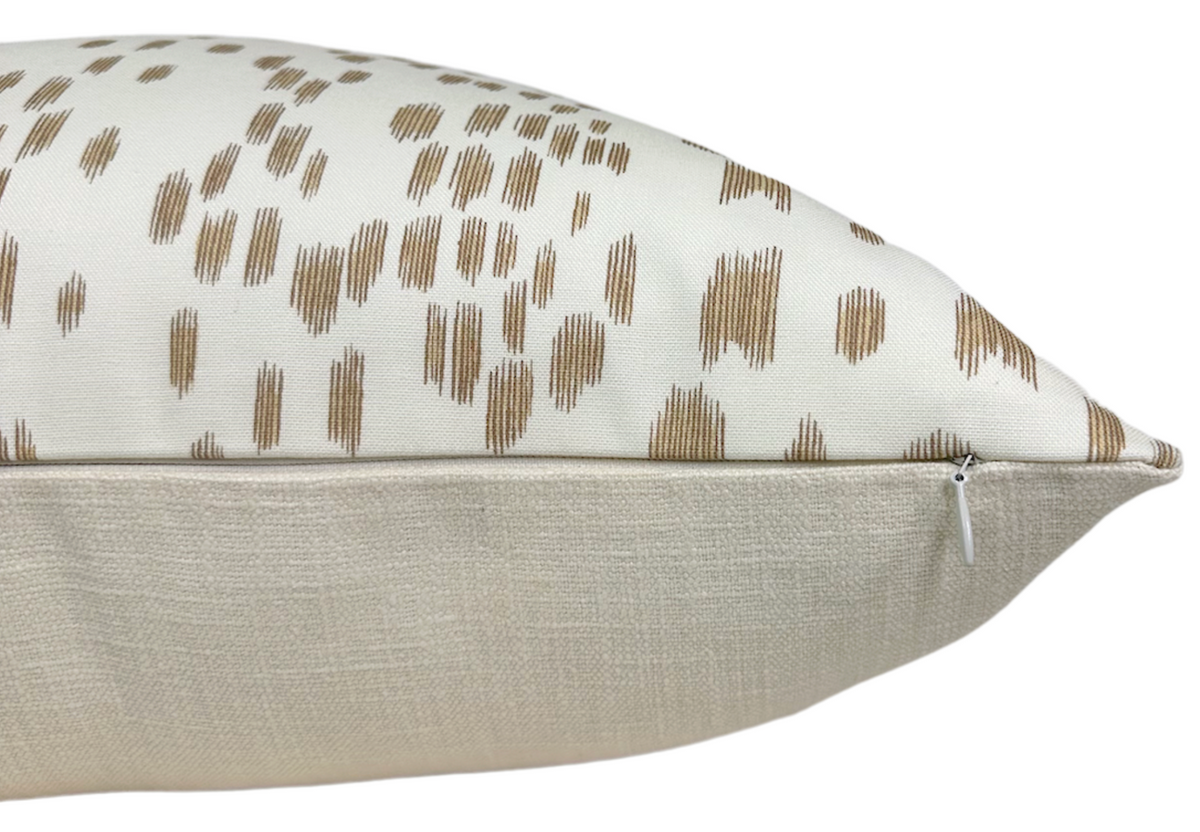 Side view of a sand-colored pillow cover featuring textured beige fabric on the bottom and white fabric with scattered brown dot patterns on top, showing a visible zipper.
