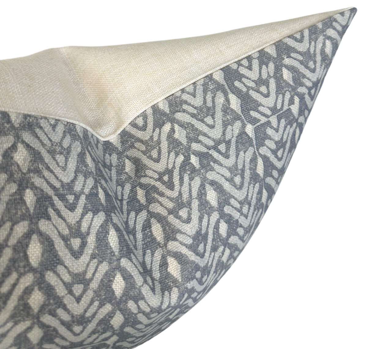 Close-up of a pillow cover corner with a beige top panel and a gray patterned lower panel featuring abstract leaf shapes in cream on the sides.