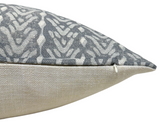 Close-up of a pillow corner with a patterned gray and white fabric on top and a plain textured beige fabric on the bottom, showing a small white zipper pull.