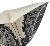Close-up of a beige pillow cover with a bold black botanical print featuring detailed leaves and star shapes on a linen-like fabric.