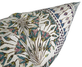 Close-up of pillow corner featuring intricate floral and geometric patterns in muted eggplant purple, teal, olive green, and white threads on textured fabric.