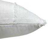 Close-up of an ivory pillow cover corner featuring textured embroidery with small fringes along the seam and a smooth fabric back panel.