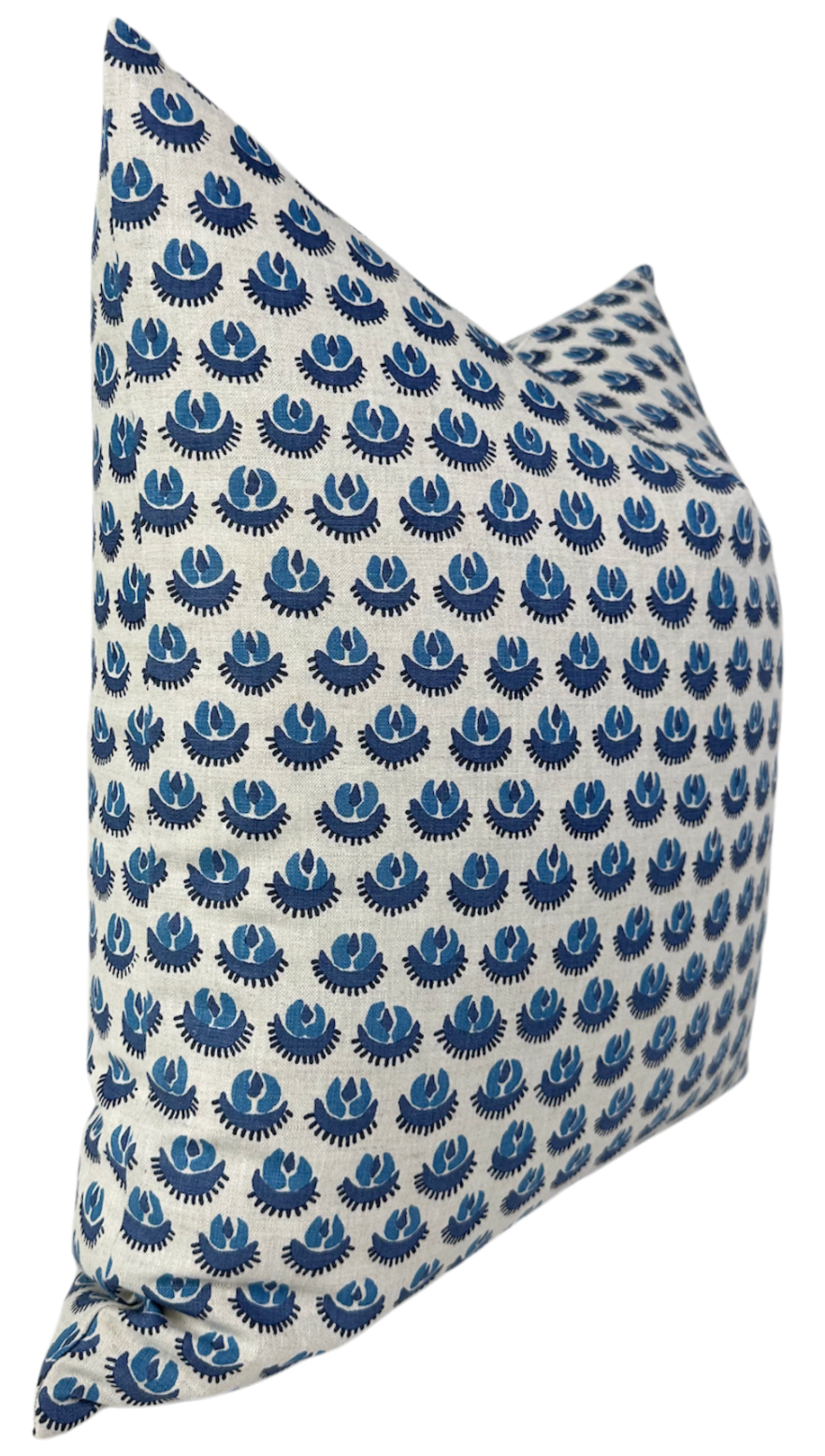 Square pillow cover with a repeating pattern of blue circular floral motifs on a white background, shown at an angle highlighting its corner and texture.