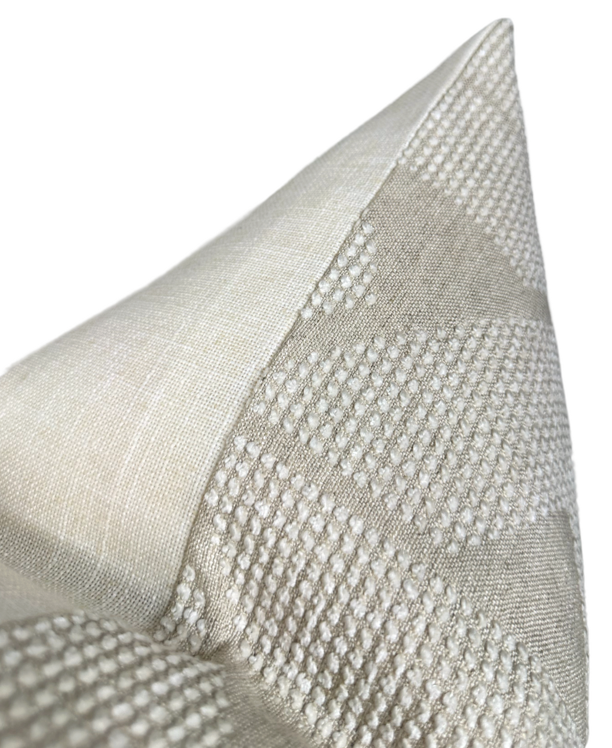 Close-up of a beige and off-white pillow cover with textured geometric patterns and smooth fabric sections meeting at a sharp corner.