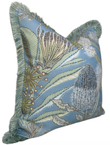 Square pillow with spa blue background featuring detailed botanical protea and leaf patterns in green, beige, and white, bordered by soft blue-green fringed trim.
