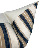 Close-up of a Shoreline pillow cover in Pebble showing textured fabric with alternating vertical stripes in navy blue, tan, and off-white, folded to reveal plain off-white reverse.