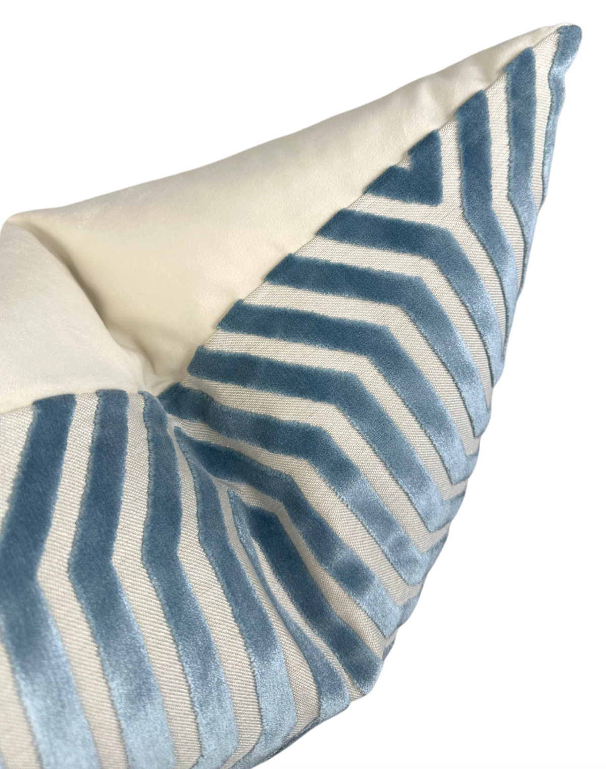 Close-up of a pillow cover with marine blue velvet chevron stripes contrasting against a smooth, cream-colored fabric background.