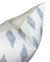 Close-up of a white pillow cover with blue diamond-shaped patterns and a beige fabric corner, shown at an angled perspective.