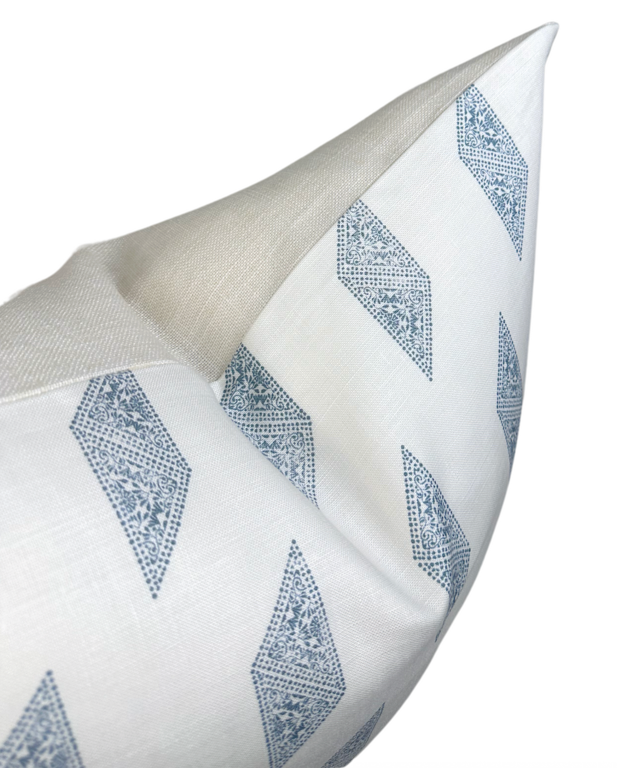 Close-up of a white pillow cover with blue diamond-shaped patterns and a beige fabric corner, shown at an angled perspective.