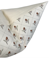 Cream pillow cover with a removable flap revealing a white underside patterned with brown pinecone and green sprig motifs arranged in diamond shapes.