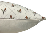 Cream-colored pillow cover with a pattern of brown acorns and green leaves arranged in a diamond grid above a plain textured beige fabric