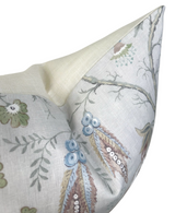 Corner of a blue and beige floral patterned pillow cover with branches, leaves, and small flowers on a light linen background.