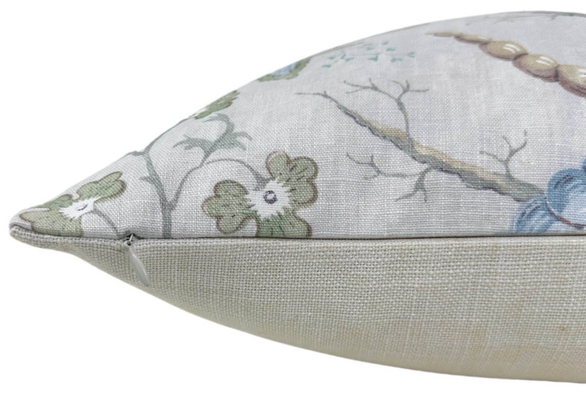 Close-up of a pillow corner with a pale blue background featuring a floral and branch pattern in muted green, blue, and beige tones.