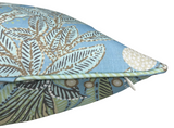 Close-up of a pillow corner with a pale blue background featuring detailed brown and green leaf patterns and a small off-white floral accent, with a discreet white zipper pull visible.