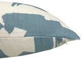 Close-up of a beige linen pillow cover with bold sky blue abstract brushstroke patterns and a visible white zipper along one edge.