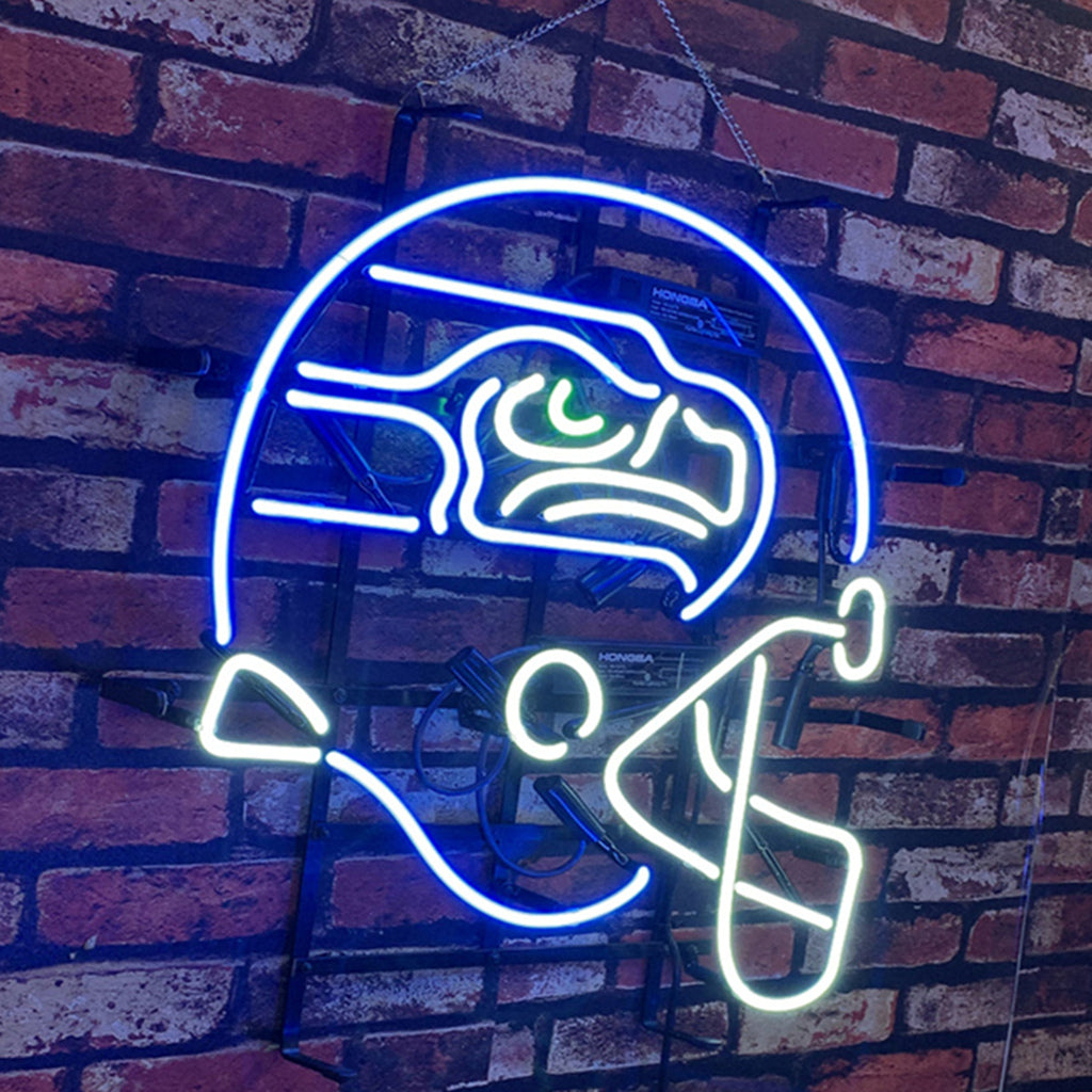 Neon sign shaped like a Seattle Seahawks football helmet with distinct blue outline, green eye detail, and white facemask illuminating against a brick wall.