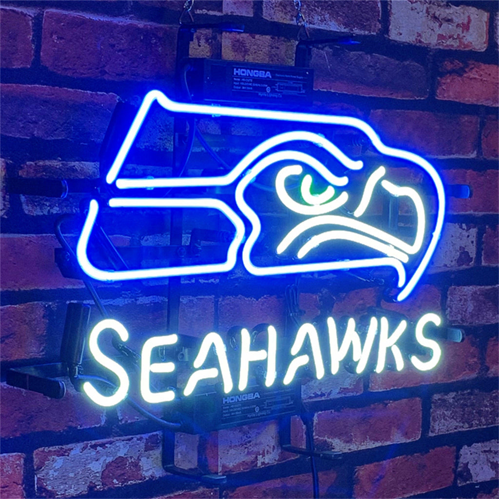 Neon sign featuring a stylized blue and white Seattle Seahawks hawk head above the word 'SEAHAWKS' in white neon, mounted on a red brick wall.