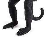 Close-up of glossy black monkey sculpture’s legs, feet with detailed toes, and curved tail curling upward against a white background.