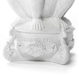 White sculpted pedestal with detailed ornate scrollwork and the inscription 'HEAR NO EVIL' beneath seated figure's feet with visible toes and nails.