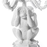 White sculpted monkey figurine sitting with hands covering its ears, detailed fur texture, part of a multi-monkey decorative arrangement with curling elements above.
