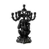Black candelabra shaped as three monkeys covering their ears, eyes, and mouth, standing on an ornate base with candle holders above them.