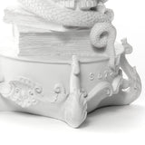 White sculptural base detail showing textured coiled serpent, ornate scrollwork, and letters 'SLT' embossed on a rounded surface.