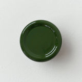 Glossy dark green circular coat hook with a concave center, mounted on a white textured wall, showing soft reflections on its surface.