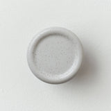 Round white ceramic coat hook with a slightly raised edge and subtle grey speckles, mounted on a white wall.