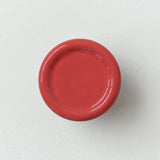 Round wall-mounted coat hook with a smooth glossy coral red finish, shown centered against a textured white wall background.
