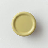 Round matte yellow coat hook with a slightly recessed center, mounted on a white textured wall, shown from the front.