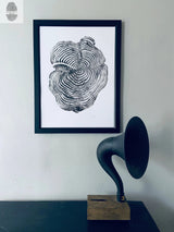 Black and white framed print of a sequoia tree cross-section with concentric growth rings, hanging above a vintage horn speaker on a wooden base against a light grey wall.