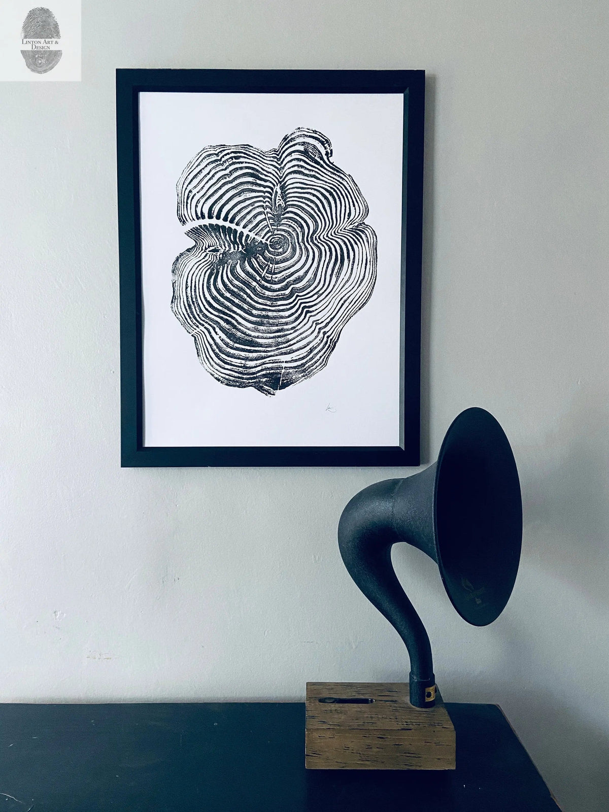 Black and white framed print of a sequoia tree cross-section with concentric growth rings, hanging above a vintage horn speaker on a wooden base against a light grey wall.