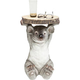 Side table featuring a realistic gray koala figure holding a round wooden top with natural bark edge, shown with a glass and glasses on the surface.