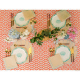 Four place settings on an orange patterned tablecloth with plates featuring a blue shell motif, gold cutlery, beige napkins, and assorted floral centerpieces including hydrangeas and pink roses.