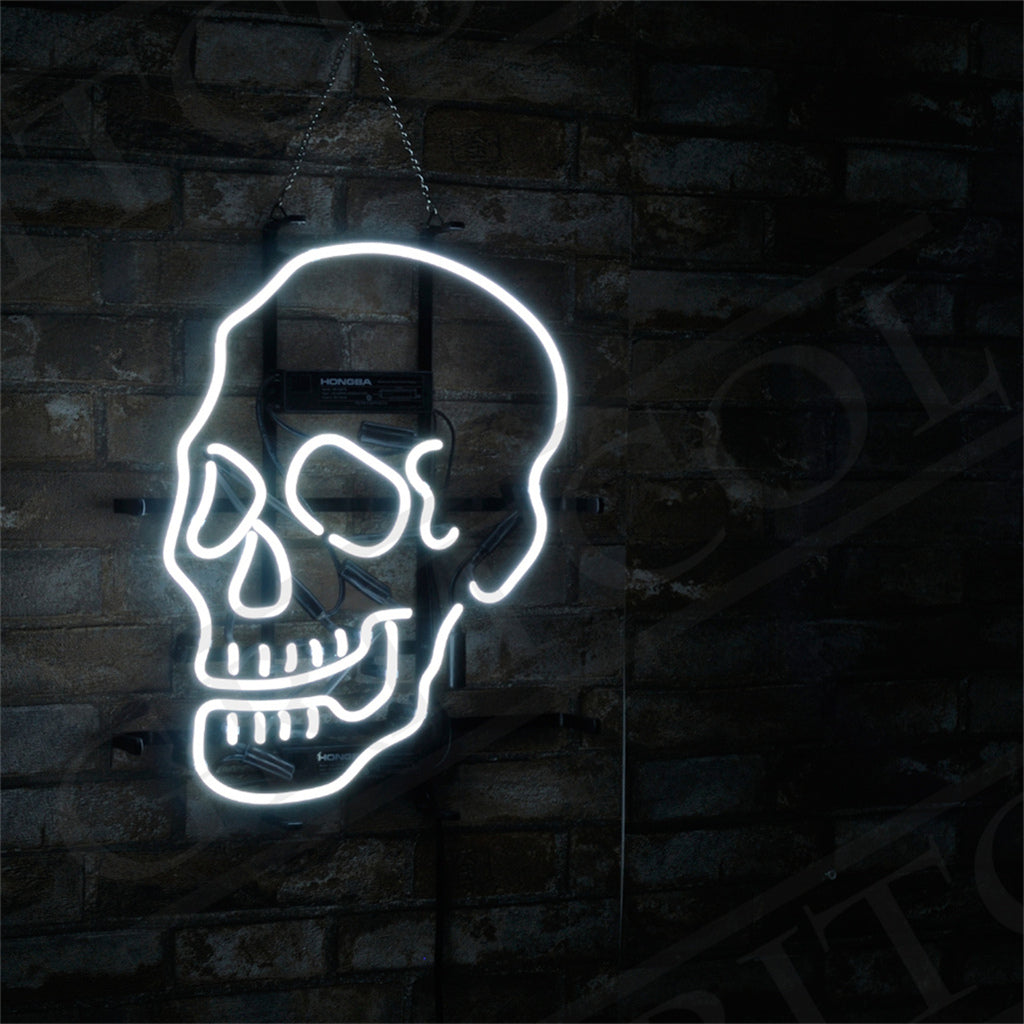 White neon light shaped like a stylized skull hanging on a dark brick wall with a metal chain, illuminating the contours and teeth details.
