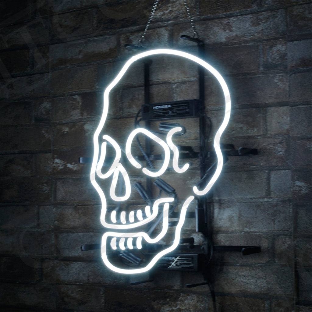 Bright white neon light shaped like a stylized human skull with hollow eye sockets and nose, mounted on a dark stone wall with visible power components behind it.