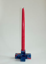 Tall red taper candle standing upright in a square, blue resin candle holder with dark and light red speckled patterns