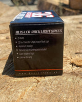 Black packaging box listing RL15 LED Rock Light specs including 15 watts, aluminum housing, Cree LEDs, mounting pads, laser logo, and lifetime warranty, on textured wood surface.