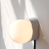 Wall-mounted sconce with a white speckled ceramic base and round frosted glass globe diffuser casting soft light and shadow on a white wall.