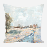Square pillow with an impressionist landscape painting featuring a pale blue sky, soft green and brown trees, and a meandering blue-gray stream across a light field.
