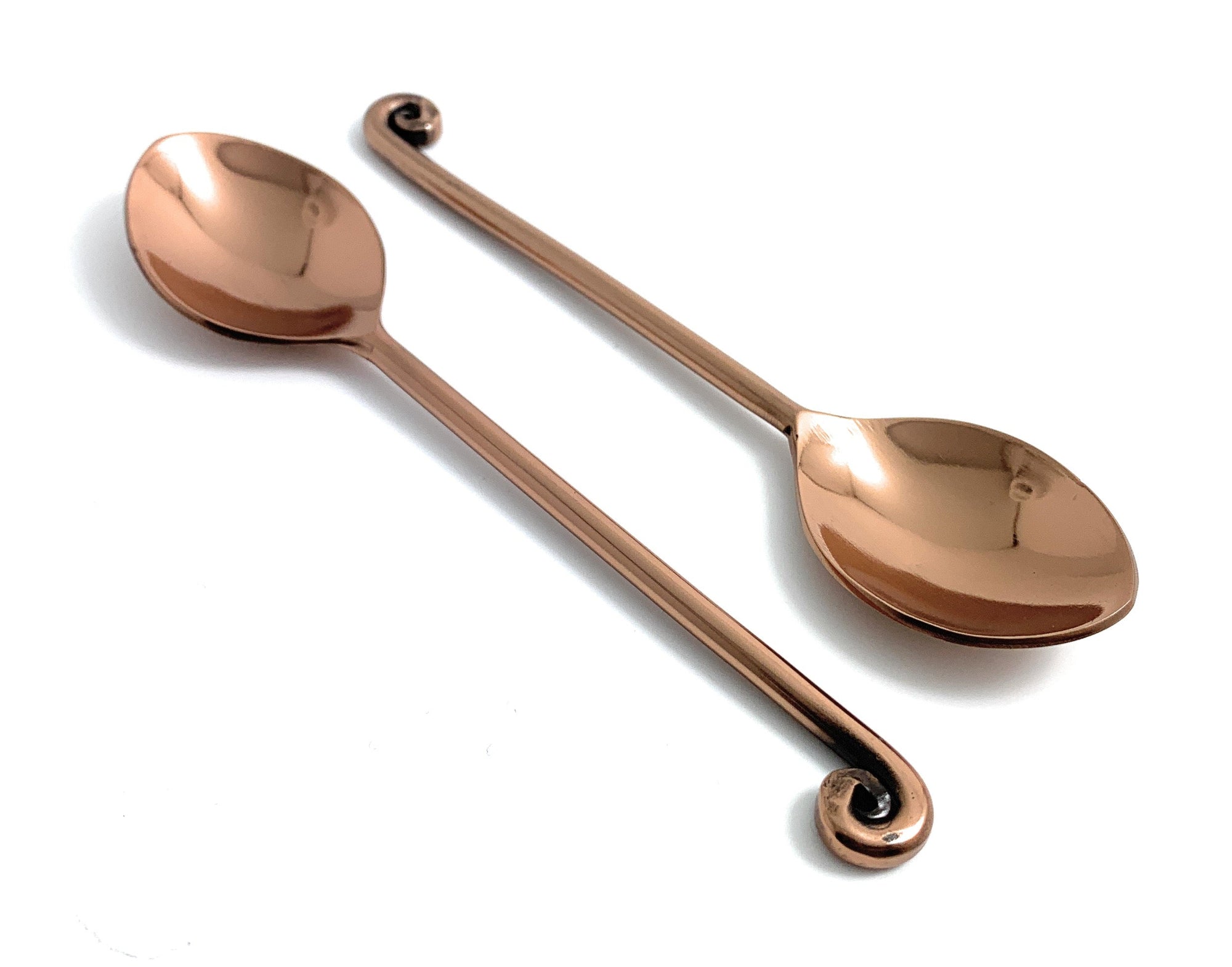 Set of six copper-coated stainless steel teaspoons with dark rose gold polish arranged on a white surface