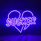 Bright purple neon sign shaped like a heart with the word 'SUCKER' across it, glowing vividly against a dark background.
