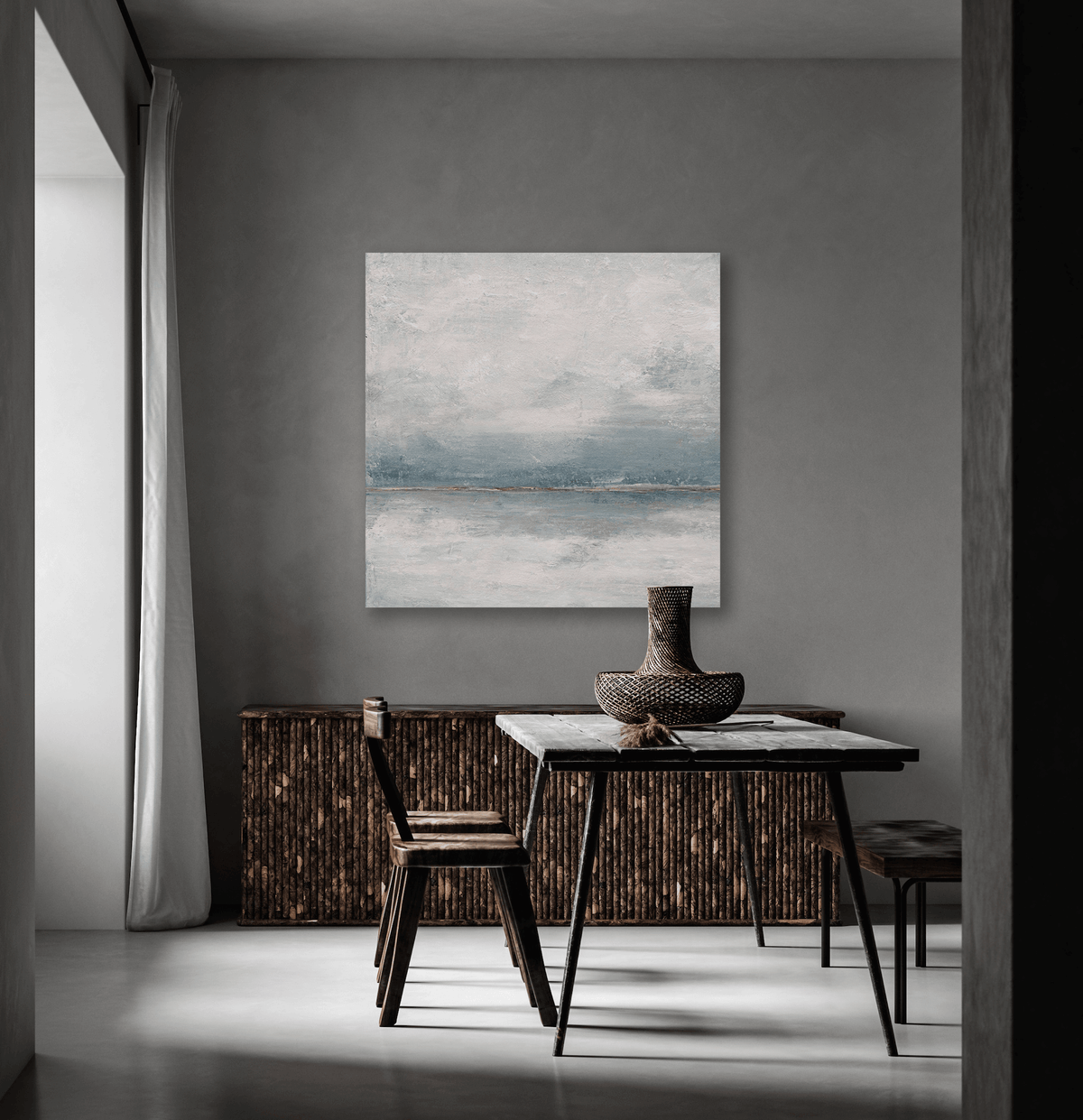 Square abstract canvas with muted blue and gray horizontal brushstrokes hangs above dark textured wood sideboard in minimalist gray room with black-legged table and chairs.