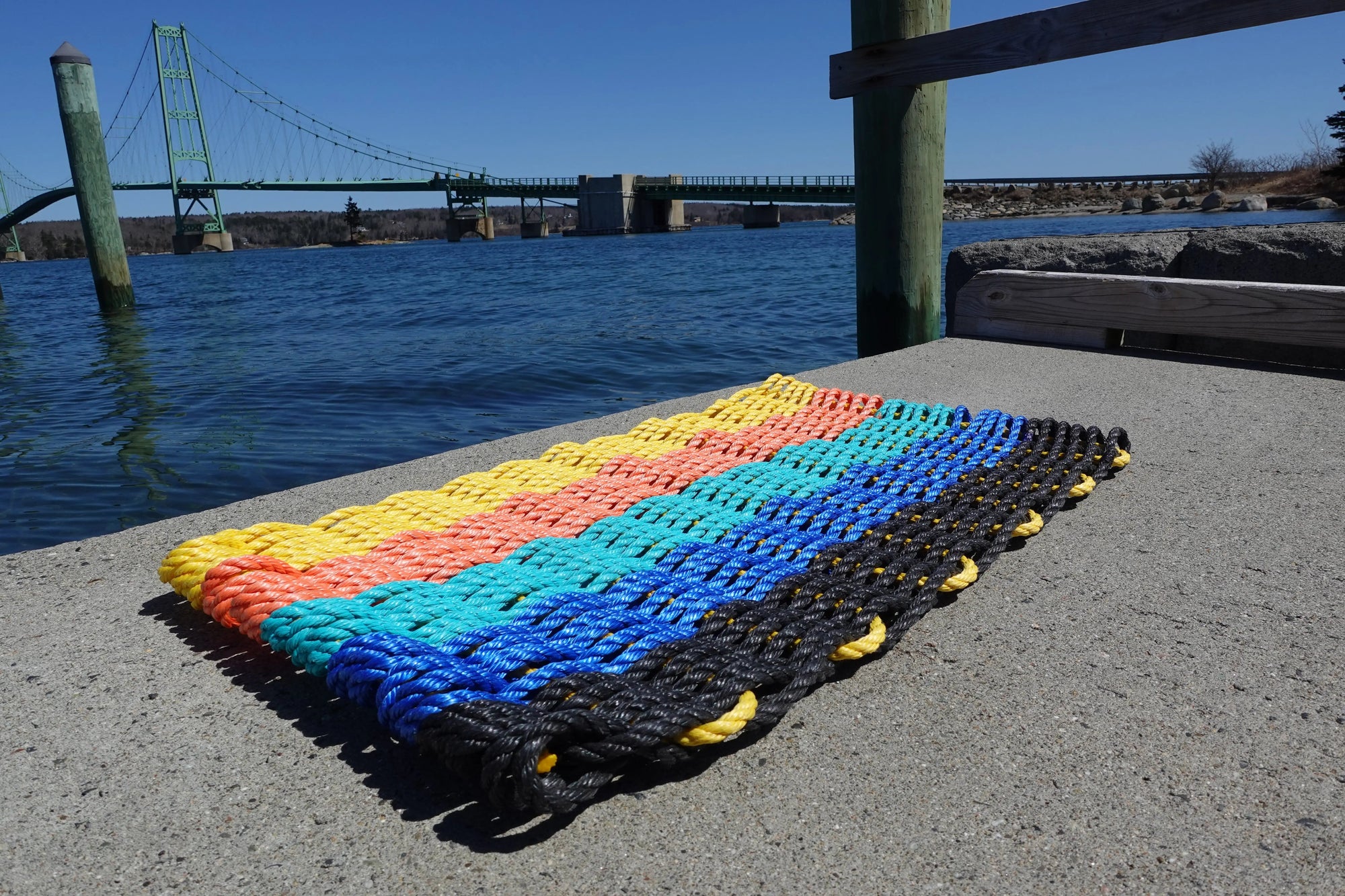 Sunset-inspired lobster rope mat with stripes of black, blue, teal, orange, and yellow