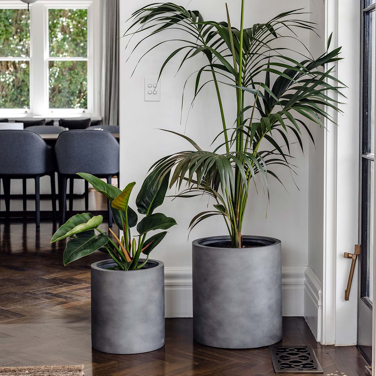 White Choob planter from The Balcony Garden US with a smooth, cylindrical shape displayed with plants in a modern porch setting