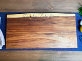 Rectangular wooden board with live edge on the top side, engraved with 'Tuckahoe Lake House Est. 2008' on a dark wooden table with a navy cloth underneath.