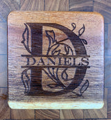 Square wooden coaster with engraved large letter D and floral design, featuring the name Daniels across the center, showcasing natural wood grain tones.